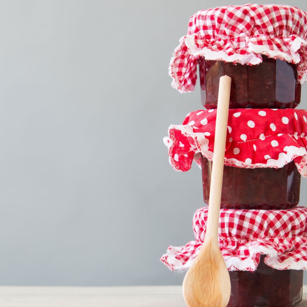 Три баночки варенья с деревянной ложкой на сером фоне