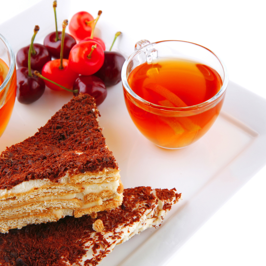 Два кусочка пирожного на столе с чаем и вишнями на белом фоне