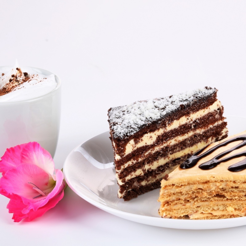 Два куска торта на столе с чашкой кофе и розовым цветком