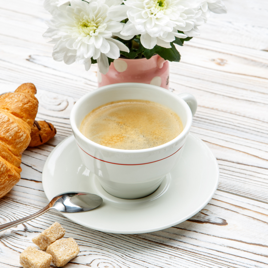 Чашка кофе и круассаны на столе с белыми хризантемами 