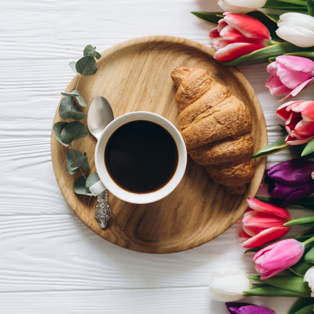 Чашка кофе с круассаном на столе с букетом тюльпанов 