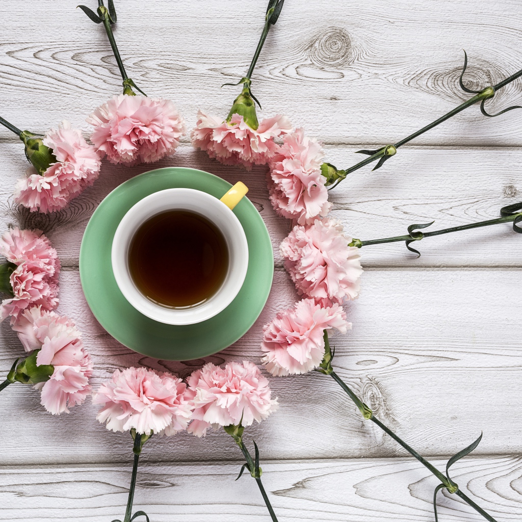 Чашка чая с розовыми гвоздиками на деревянном фоне