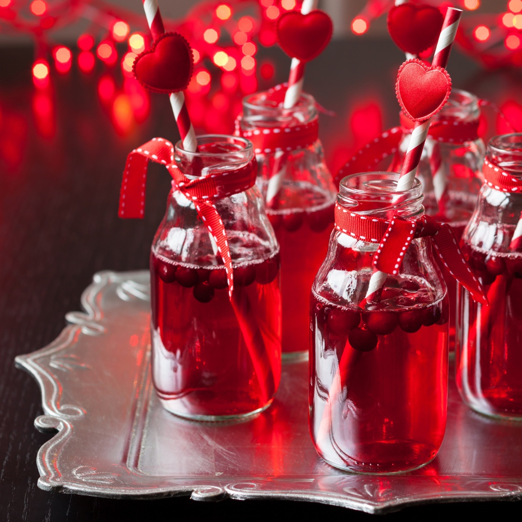 Вкусный напиток с клюквой в стеклянных бутылках на столе с трубочками