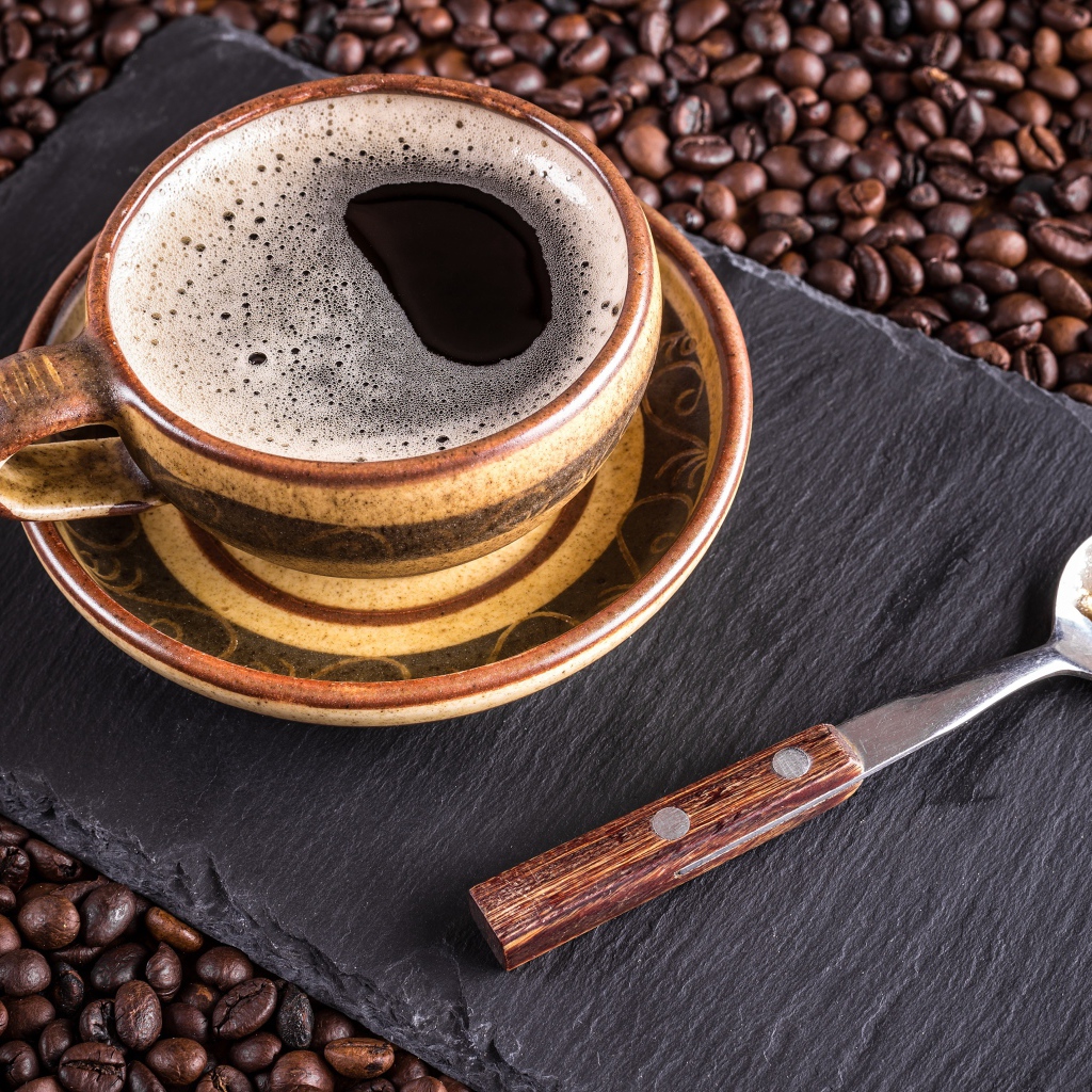 Большая чашка кофе с чайной ложкой стоят на кофейных зернах