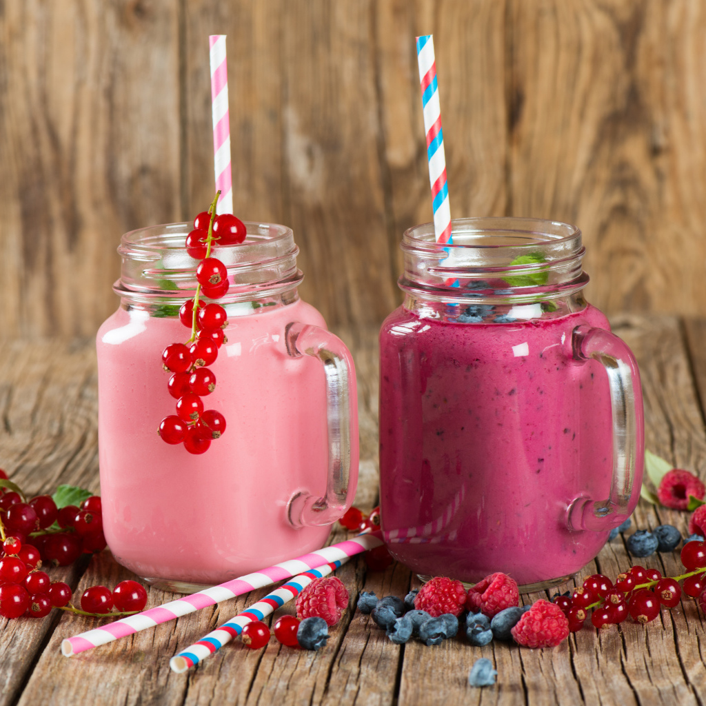 Ягодное смузи в баночках на столе со свежими ягодами малины, смородины и черники