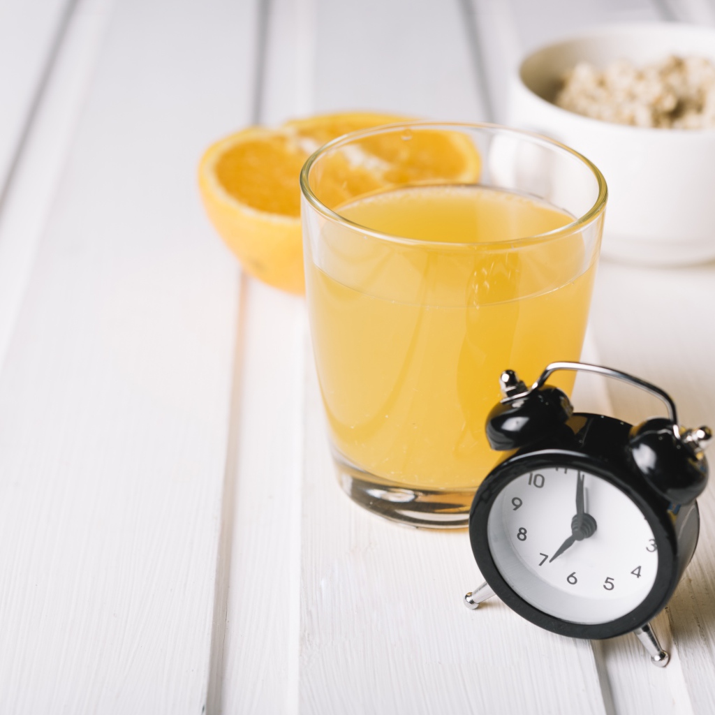 Черный будильник на столе со стаканом сока и хлопьями 