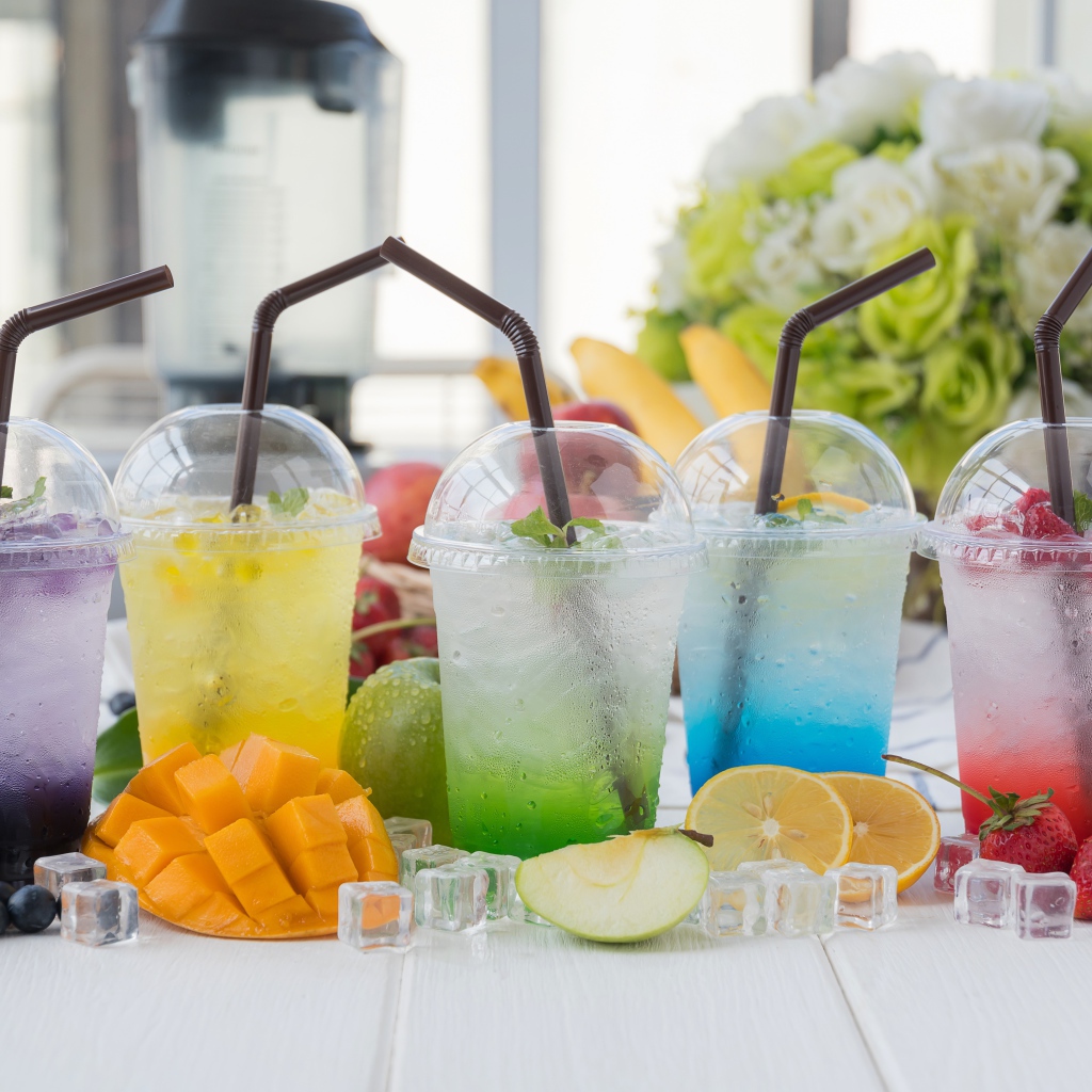 Коктейли в стаканах с трубочками на столе с кубиками льда и фруктами