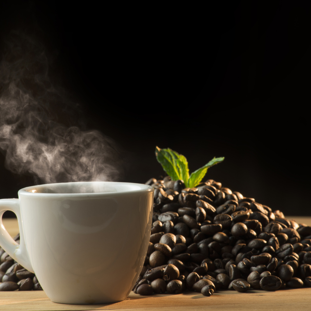 Кофейные зерна на столе с чашкой горячего кофе 