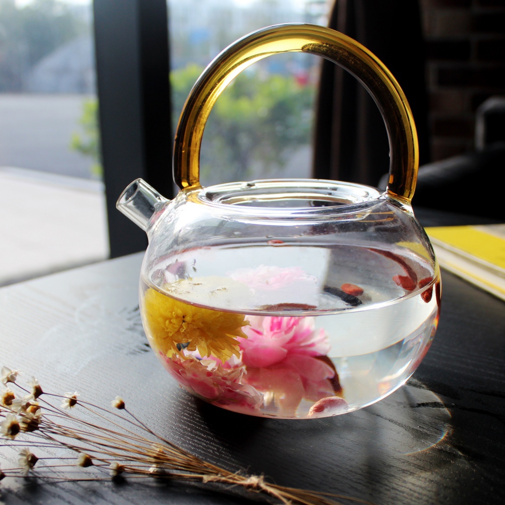 Цветочный чай в стеклянном чайнике на столе 