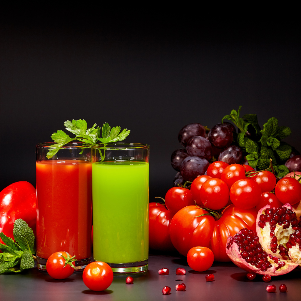 Два стакана сока на столе со свежими помидорами, перцем, гранатом, виноградом и зеленью