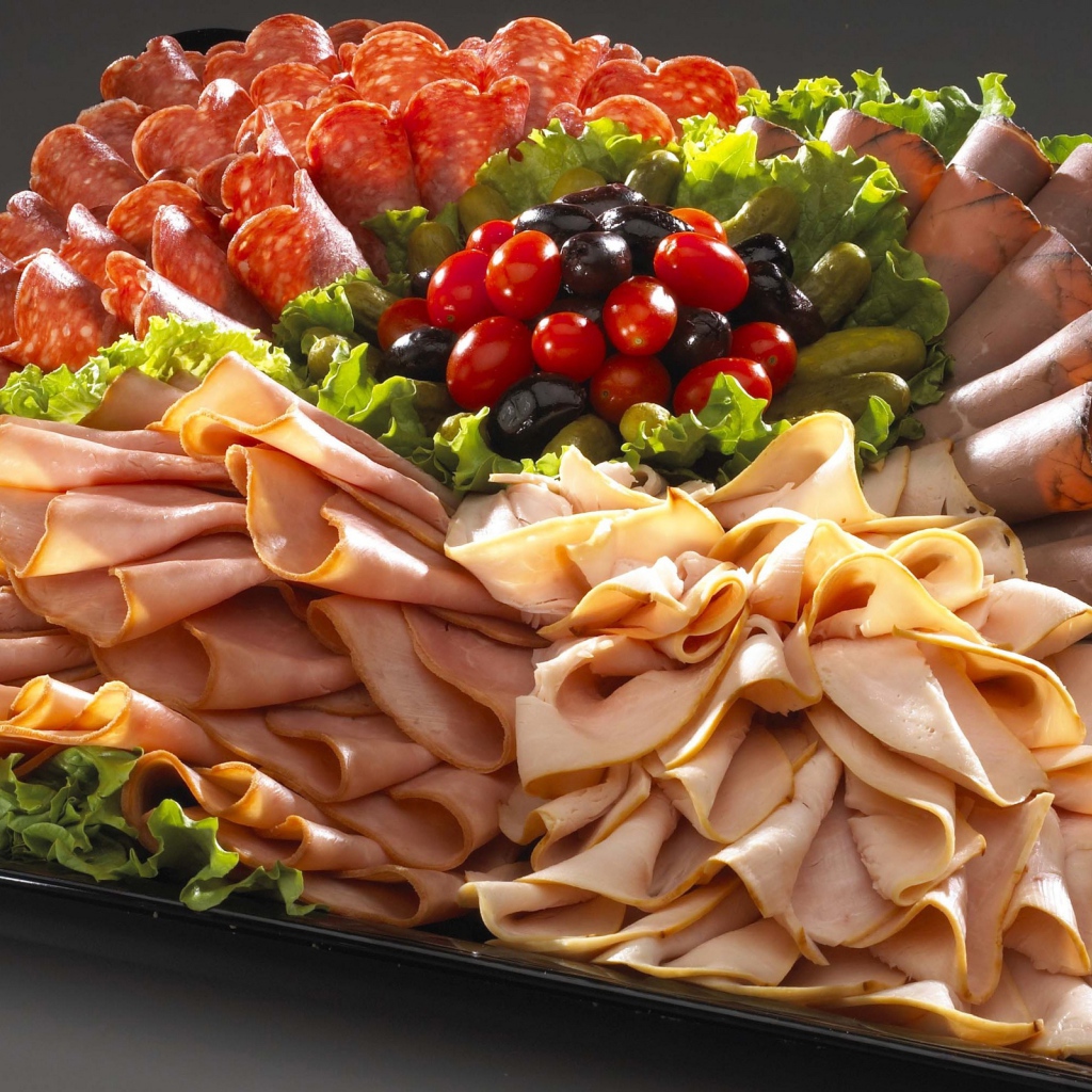 Большое блюдо с аппетитной мясной нарезкой, листьями салата и оливками