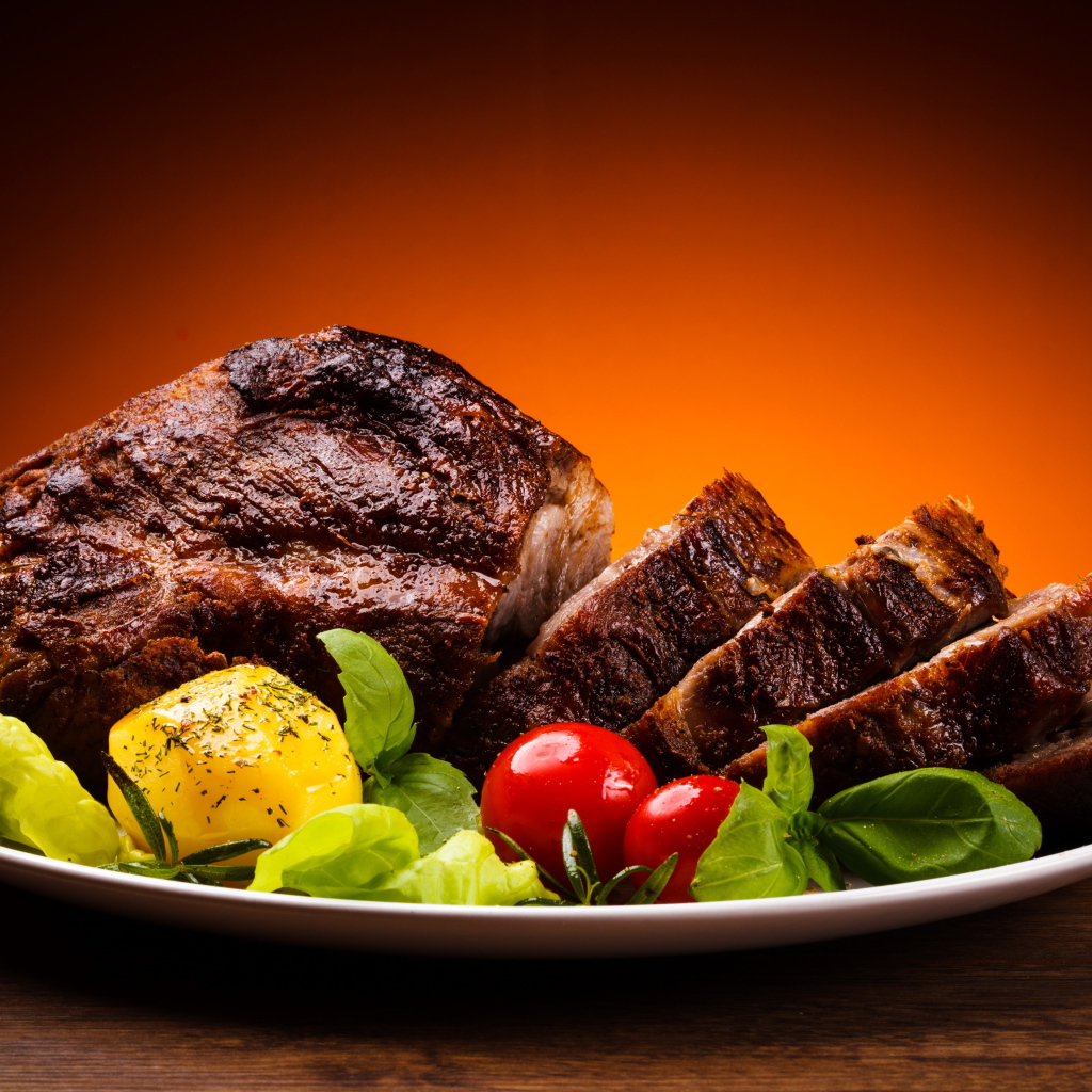 Кусок жареного мяса на тарелке с картофелем и помидорами 