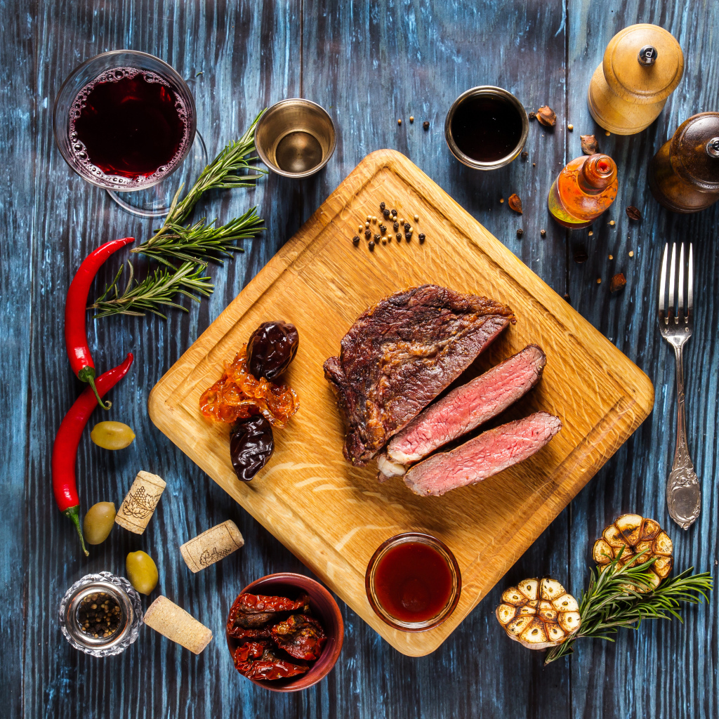 Кусок мяса на столе со специями и стаканом вина