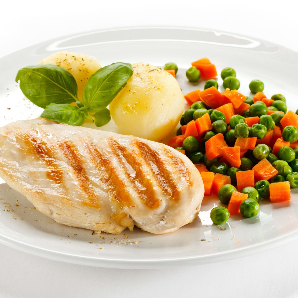 Куриная грудка на белой тарелке с картофелем, морковью и зеленым горошком