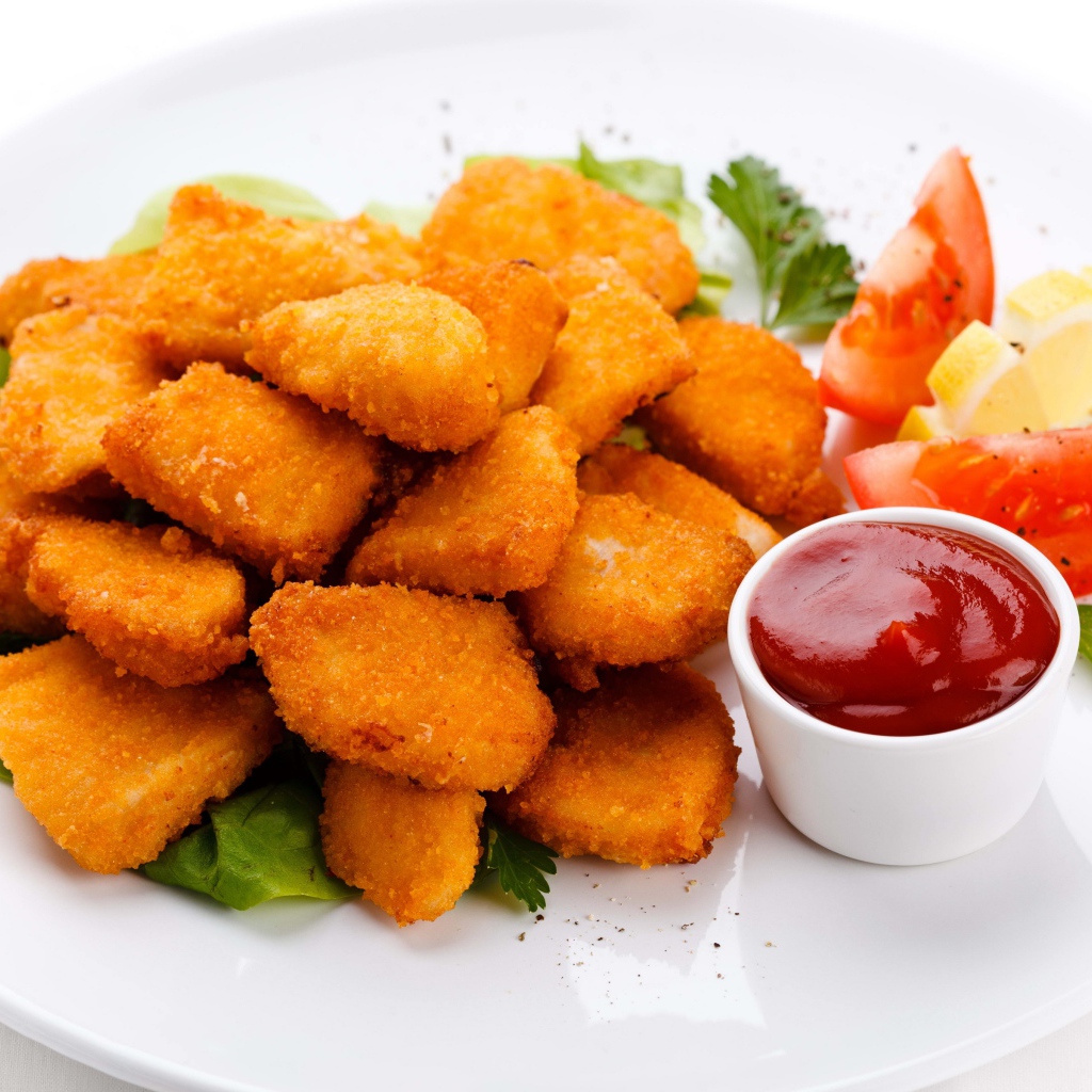 Куриные наггетсы с соусом и помидорами на белой тарелке 