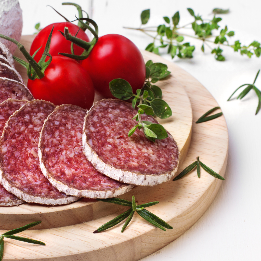 Вкусная колбаса на разделочной доске с помидорами и зеленью 