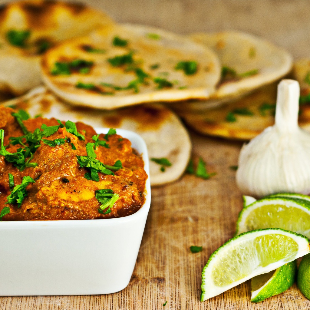 Мясное блюдо на столе с лепешками, кусочками лайма и чесноком