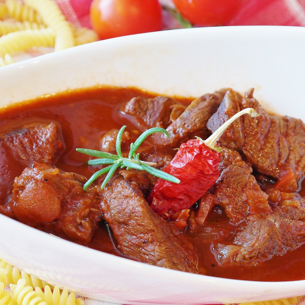 Мясной гуляш в белой тарелке с острым перцем