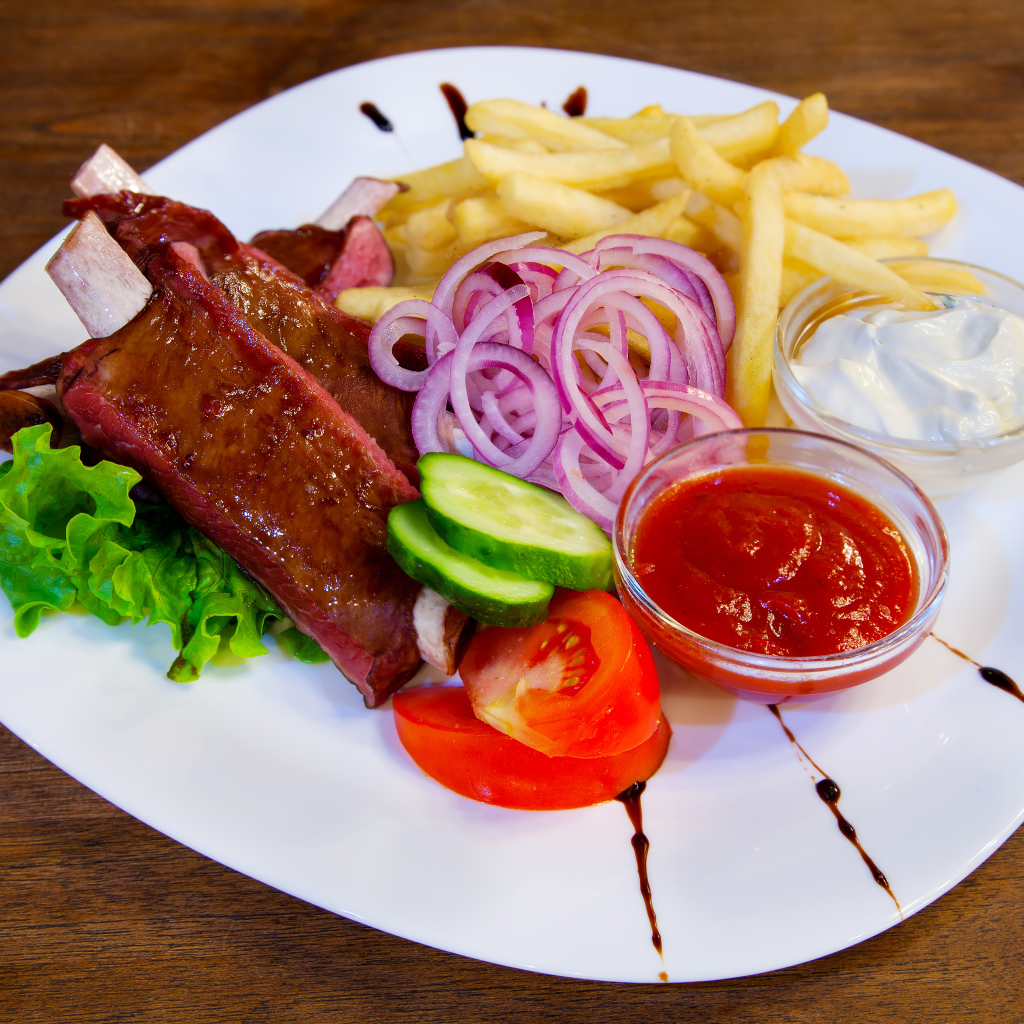 Мясо с овощами и картофелем фри на большой белой тарелке с соусом