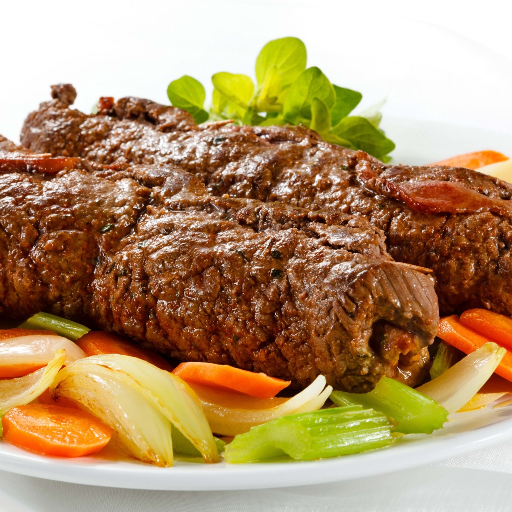 Свинина на тарелке с овощами на белом фоне