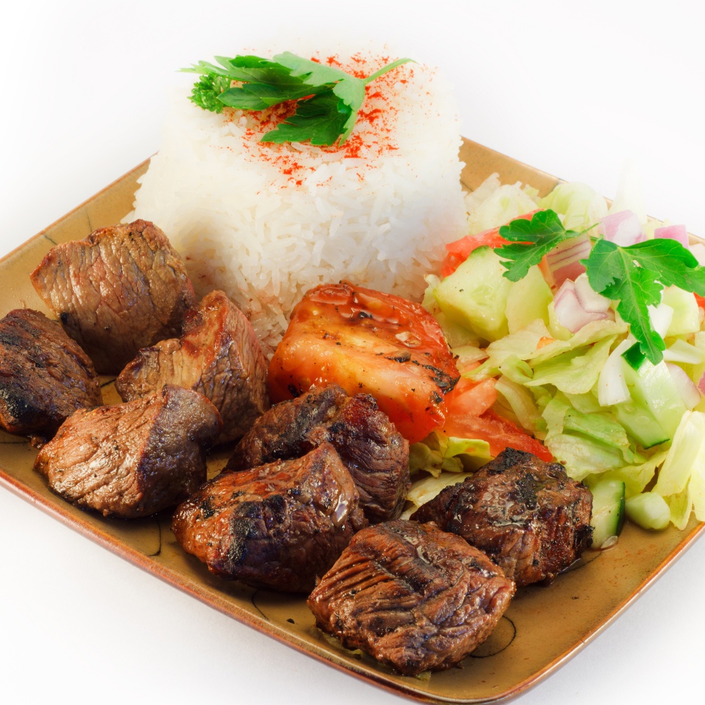 Шашлык с рисом и овощами в тарелке на белом фоне