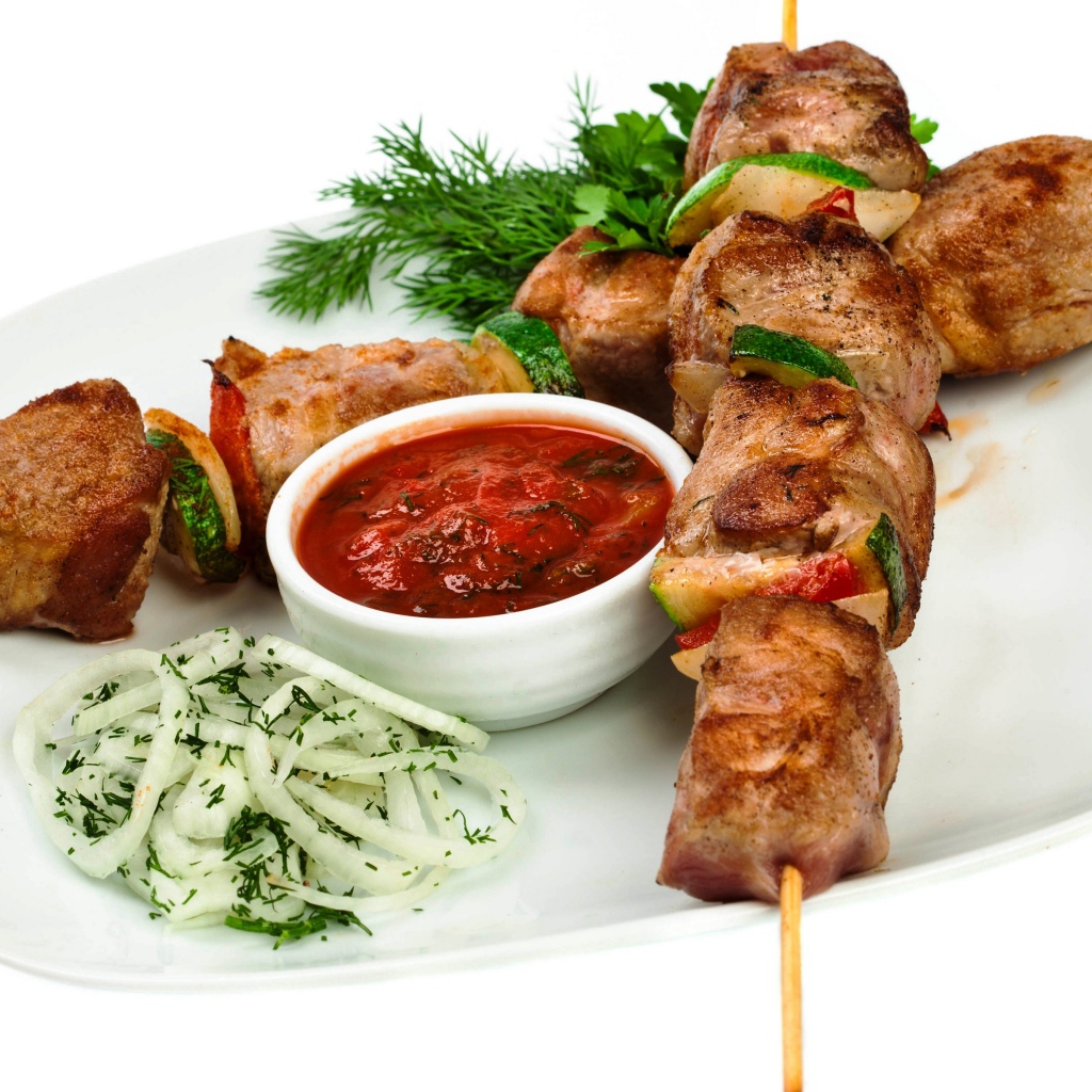 Шашлык на белой тарелке с соусом, зеленью и луком