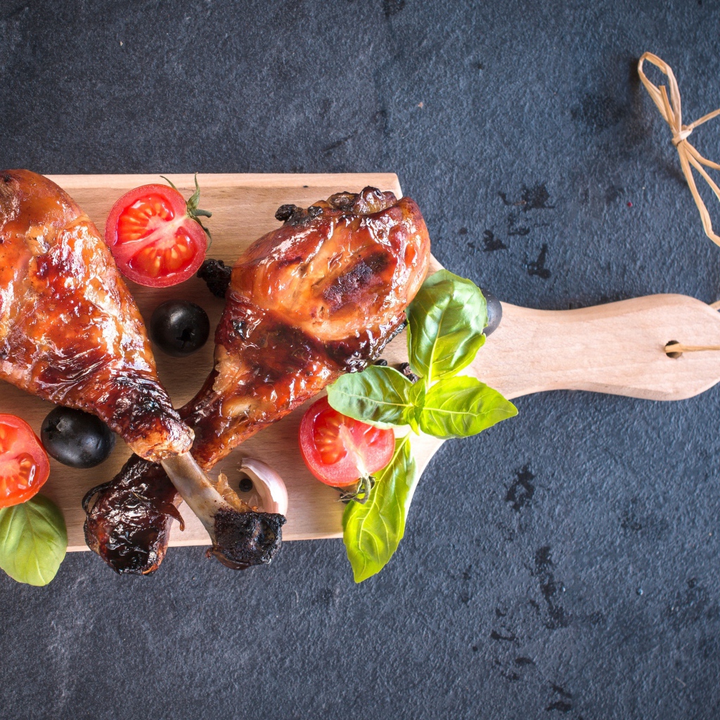 Две зажаренных куриных ножки с овощами на разделочной доске