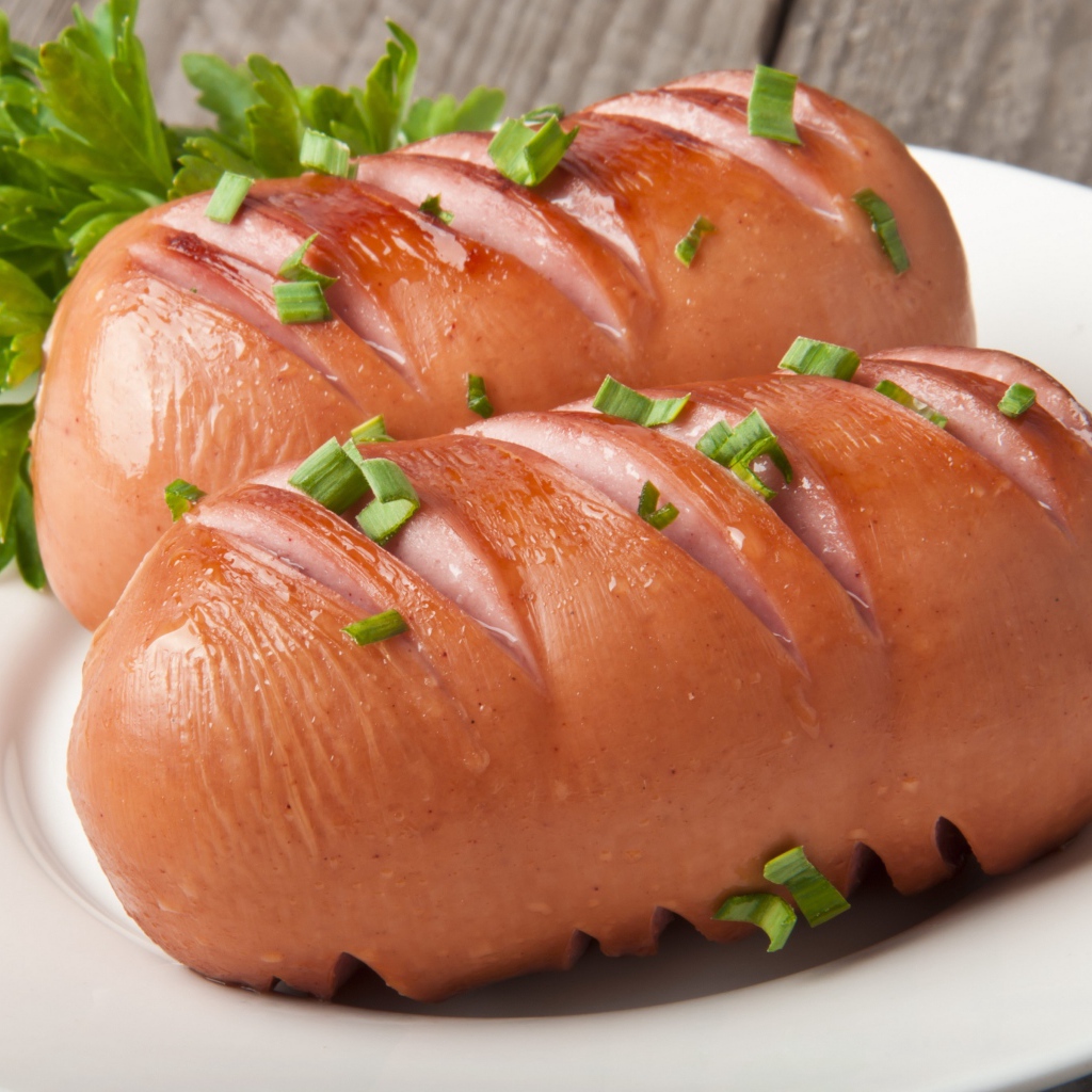 Два жареные сардельки на большой белой тарелке с зеленью 