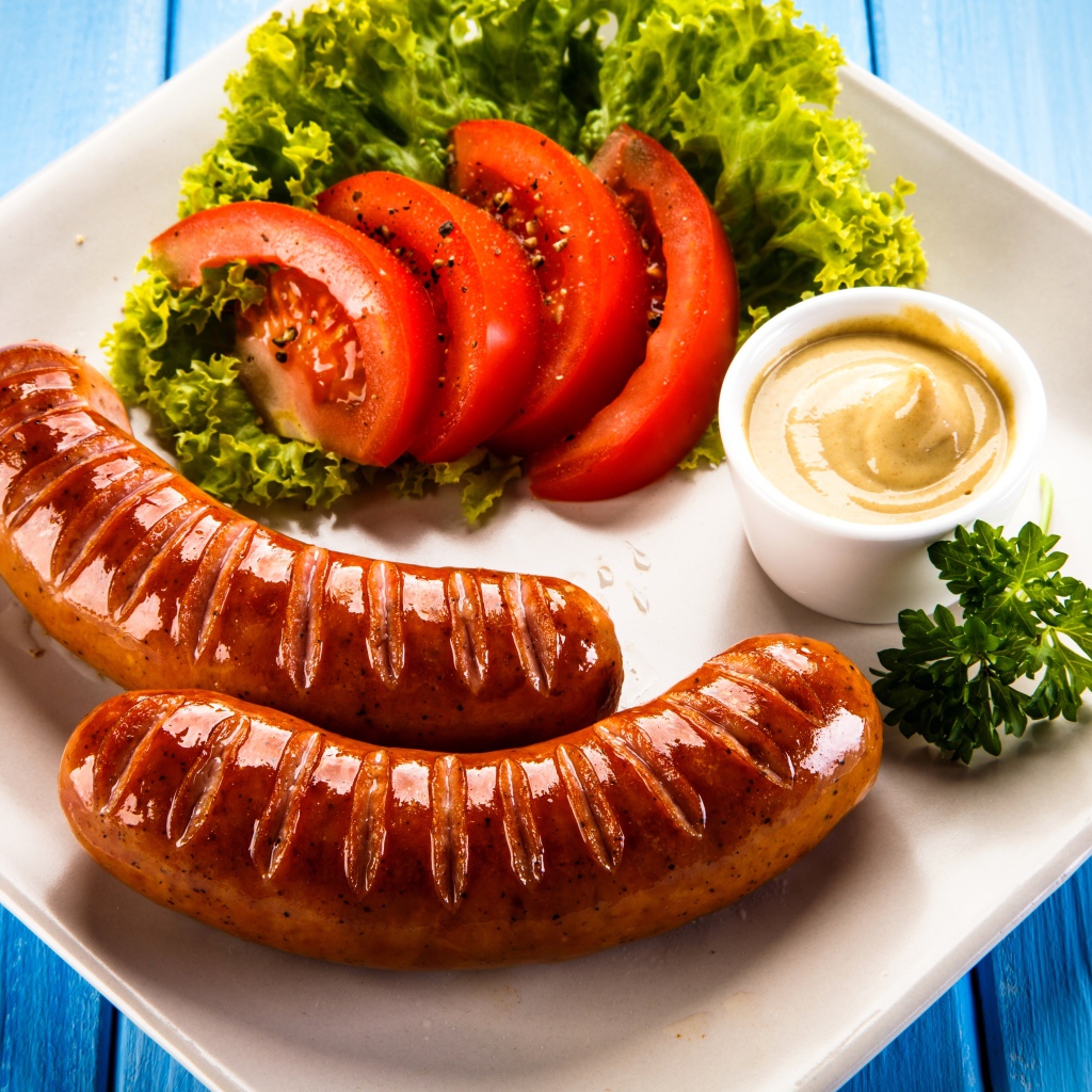 Две сосиски гриль на тарелке с овощами и горчицей