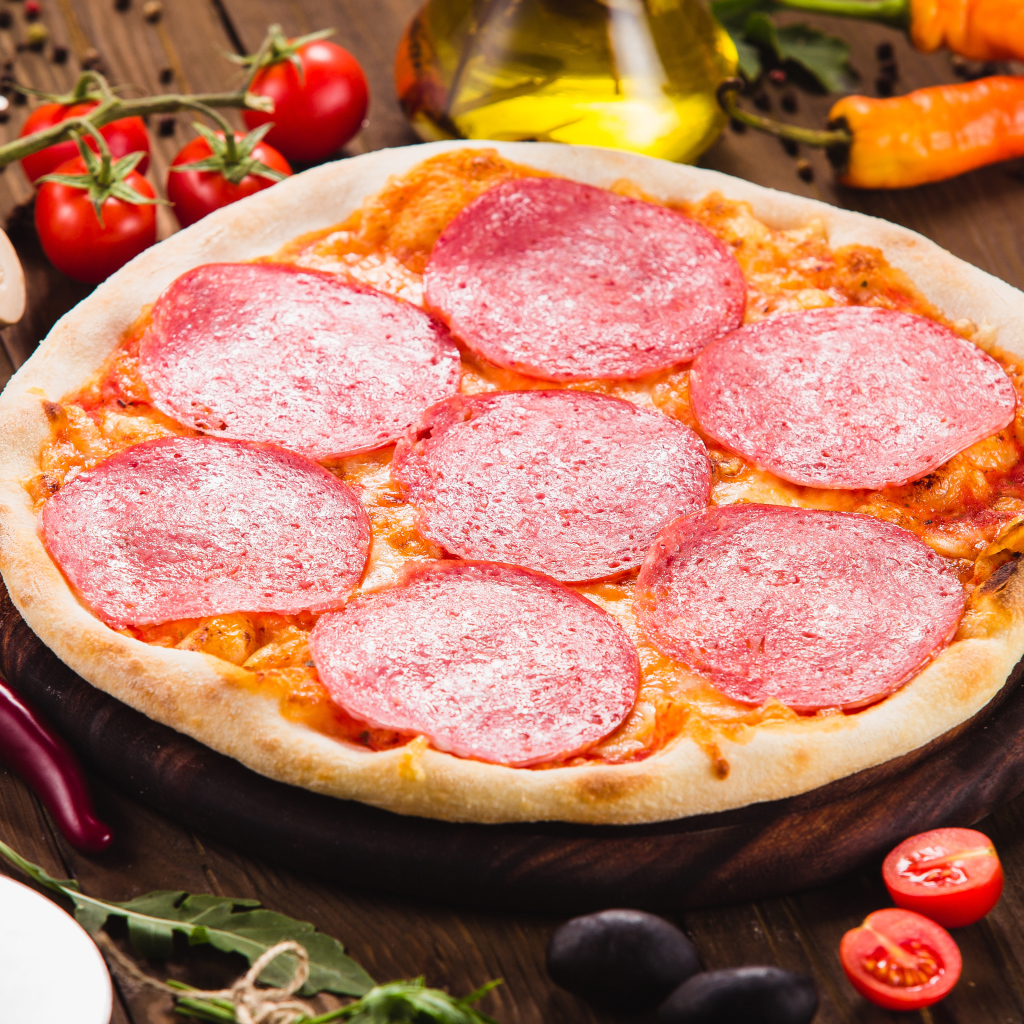 Пицца с салями на столе с овощами 