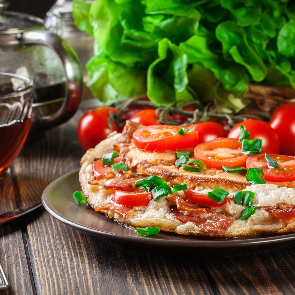 Пицца с помидорами на столе с чаем и зеленью 