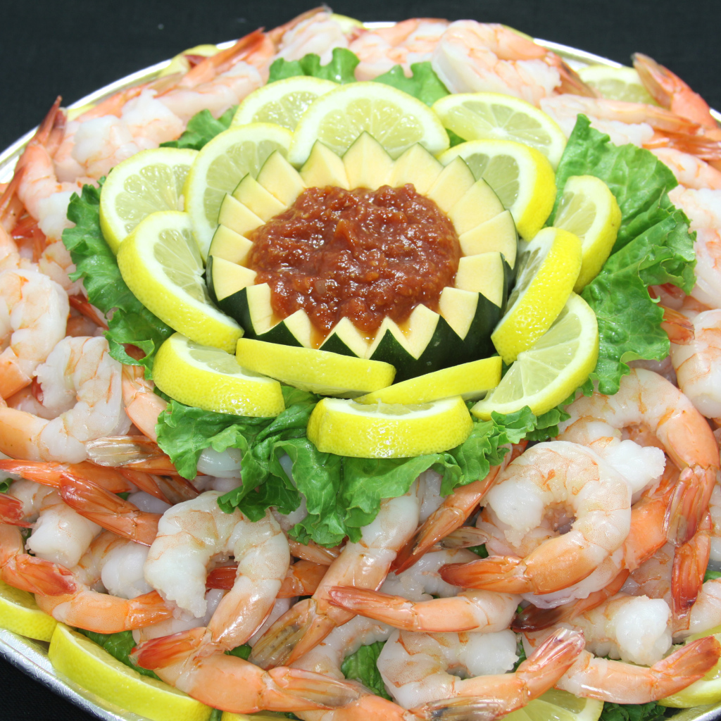 Вареные креветки с лимоном и соусом на большой тарелке