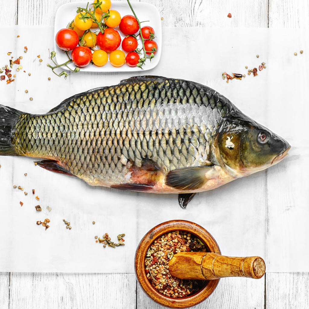 Свежий карась на столе со специями и помидорами