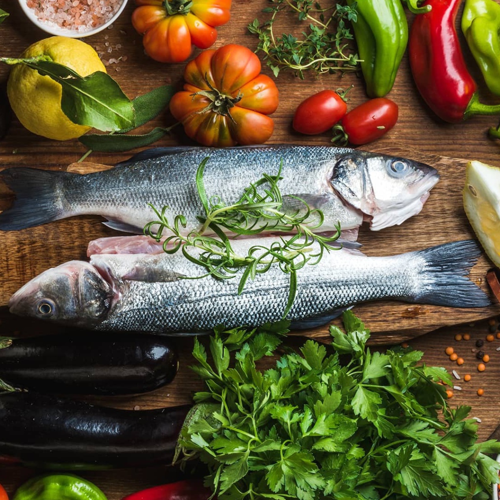 Свежая рыба на столе с овощами и зеленью 