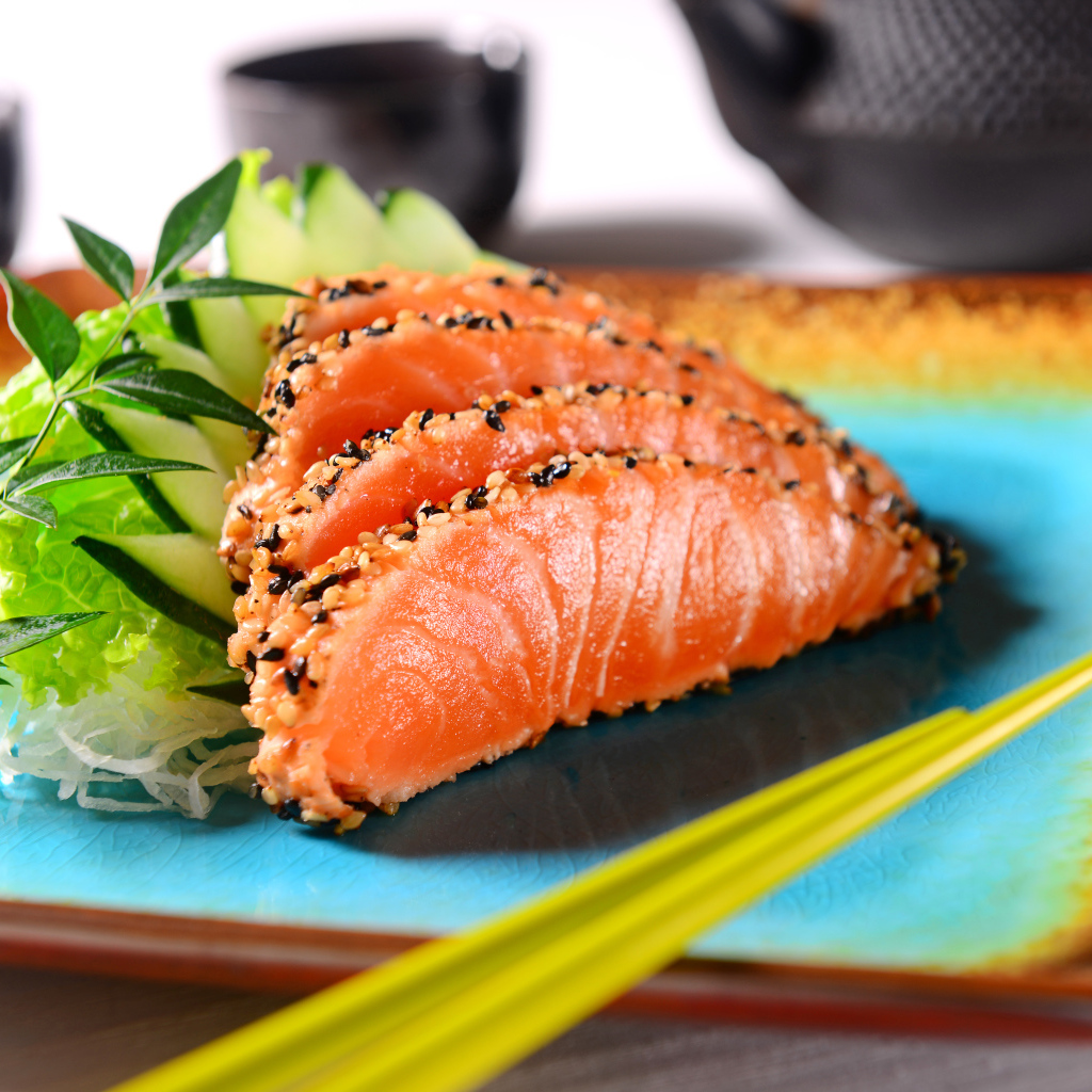 Красная рыба с листьями салата и свежими огурцами на тарелке с палочками