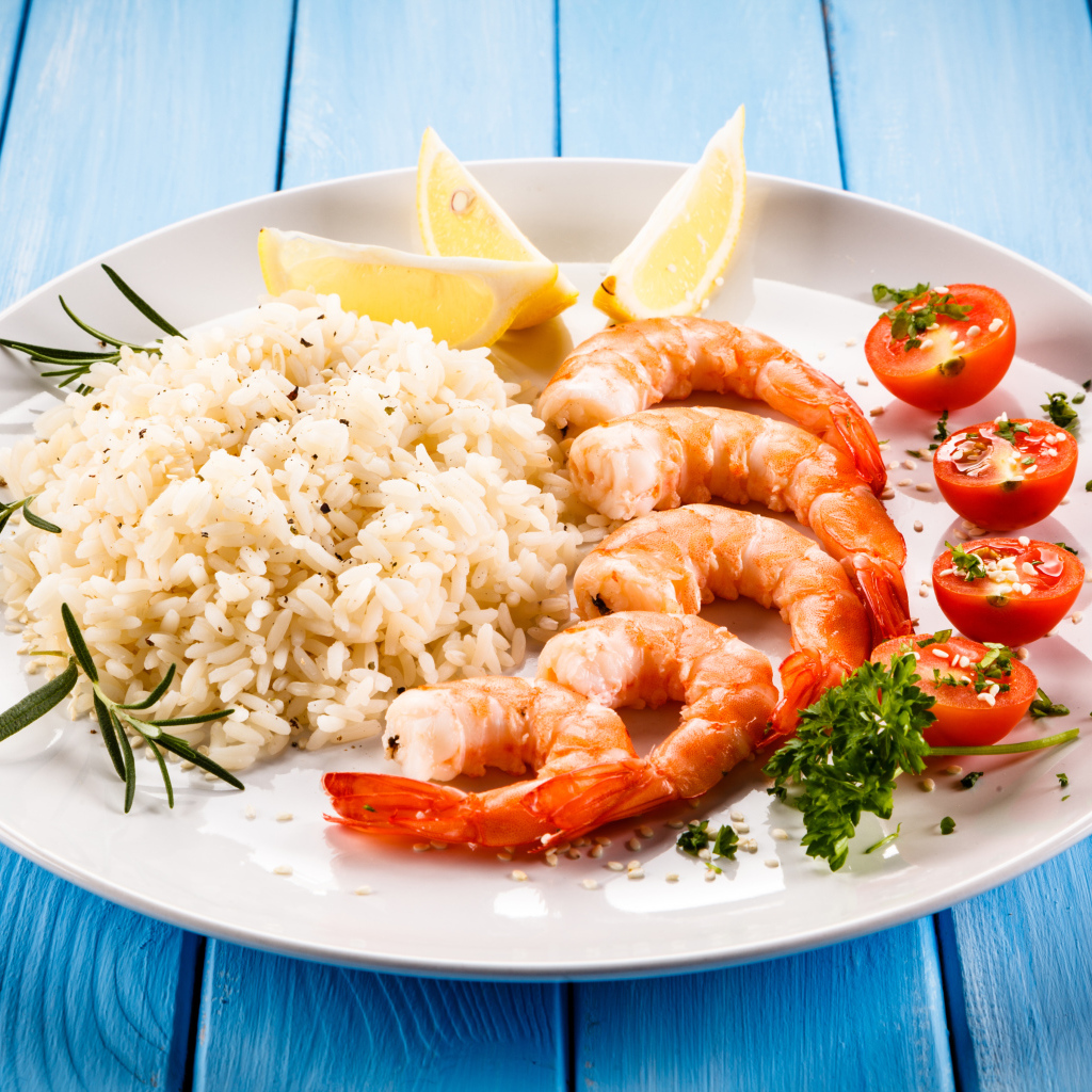 Креветки на тарелке с рисом, помидорами и лимоном