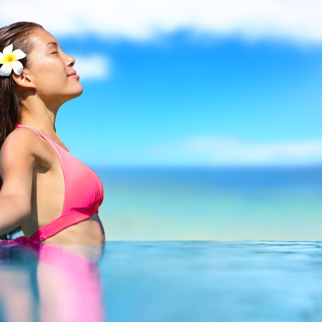 Девушка в розовом купальнике стоит в воде на солнце