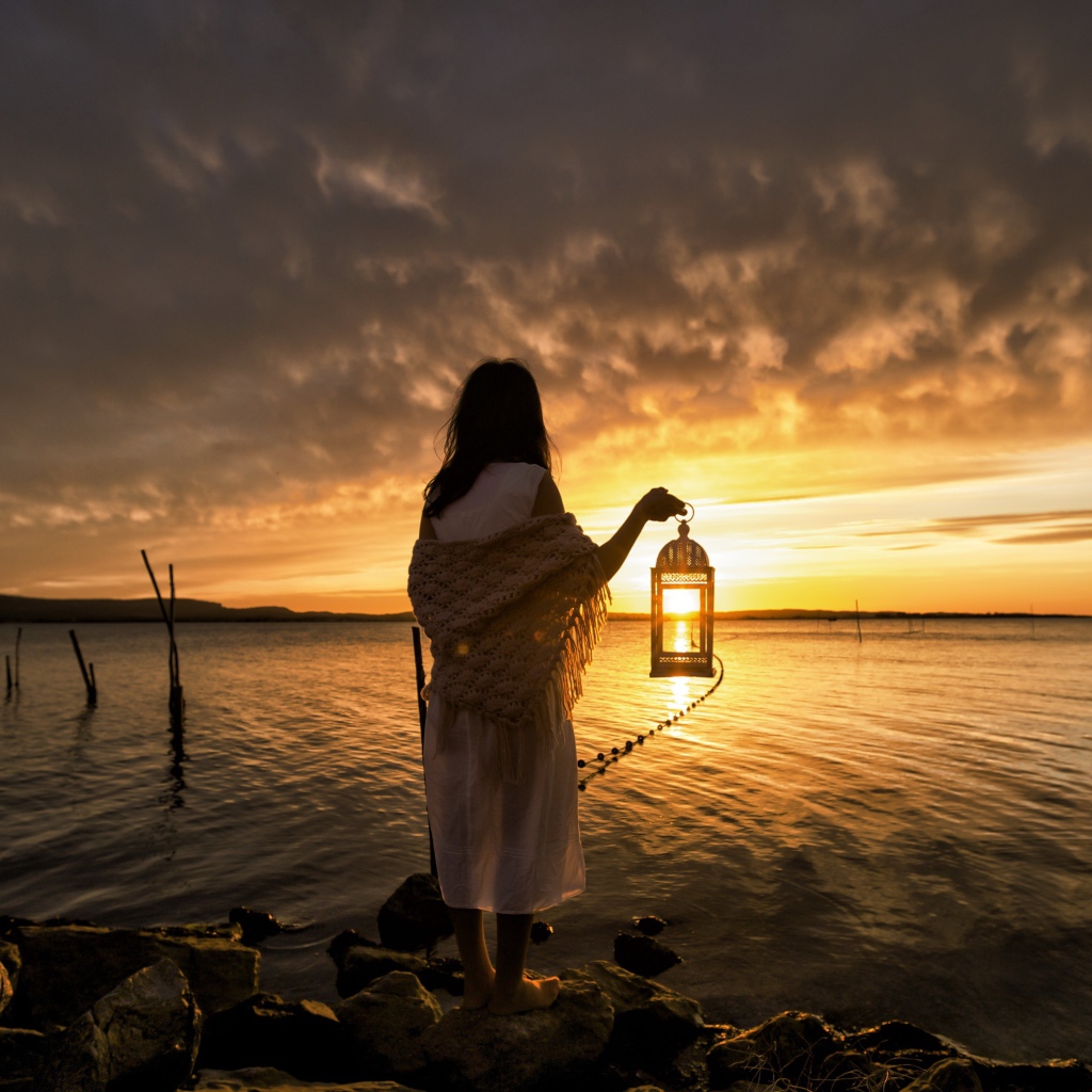 Девушка в белом платье стоит у воды с фонарем