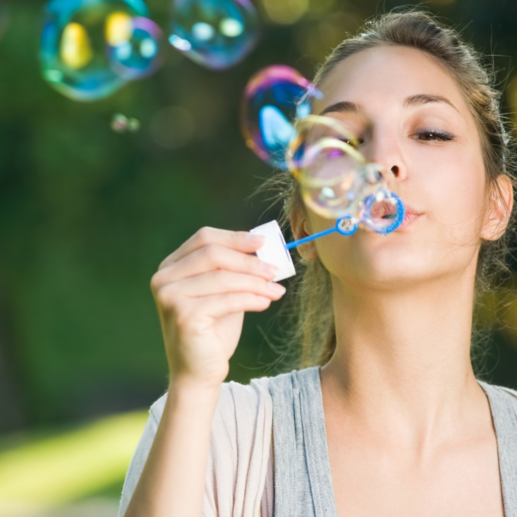 Милая молодая девушка пускает мыльные пузыри