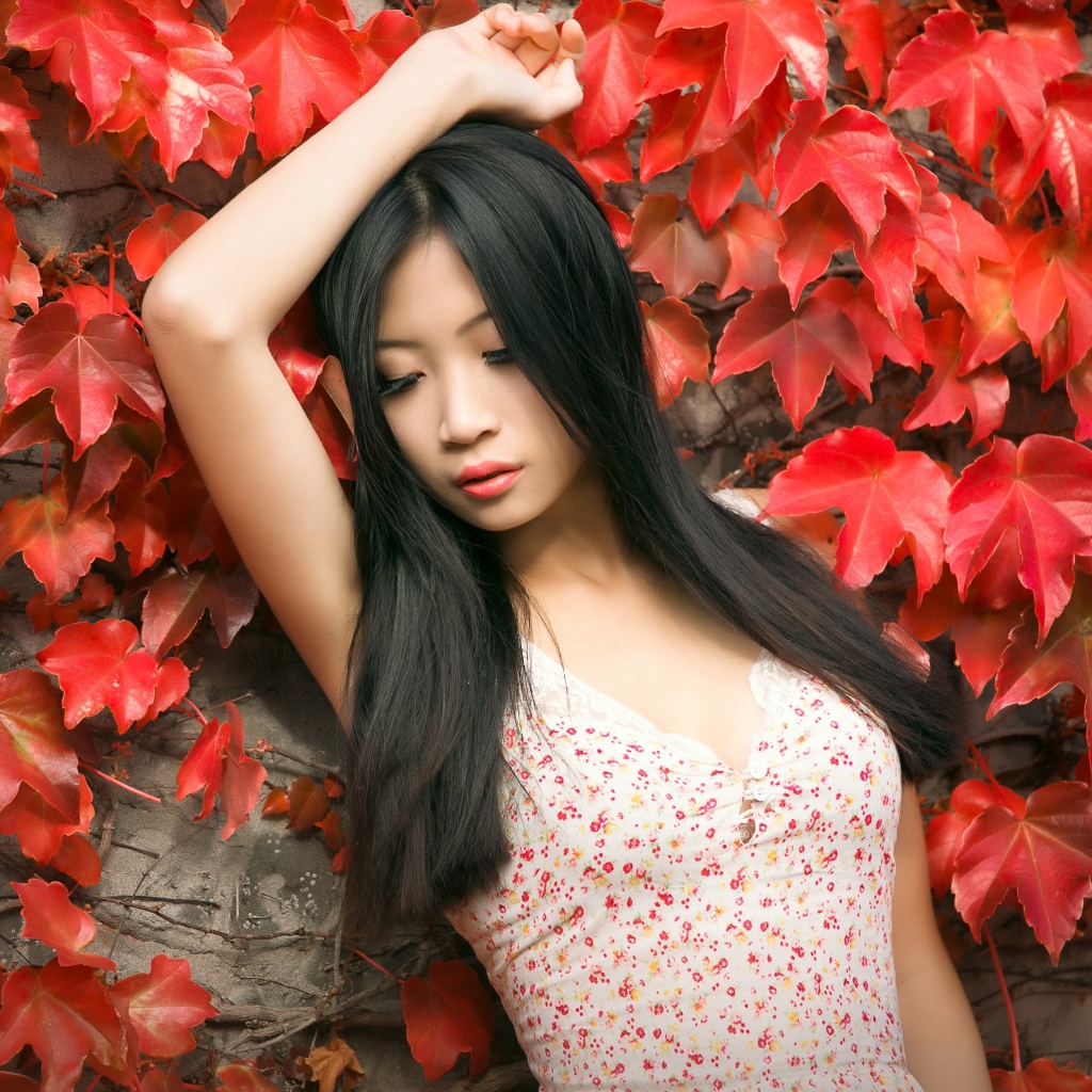 Молодая девушка азиатка стоит у стены с красными листьями