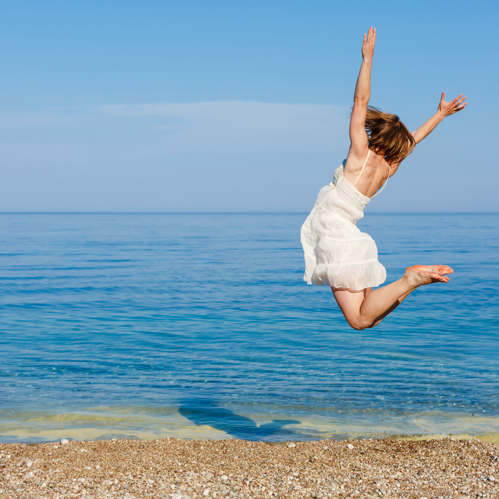 Молодая девушка в белом платье делаем прыжок на песке у моря