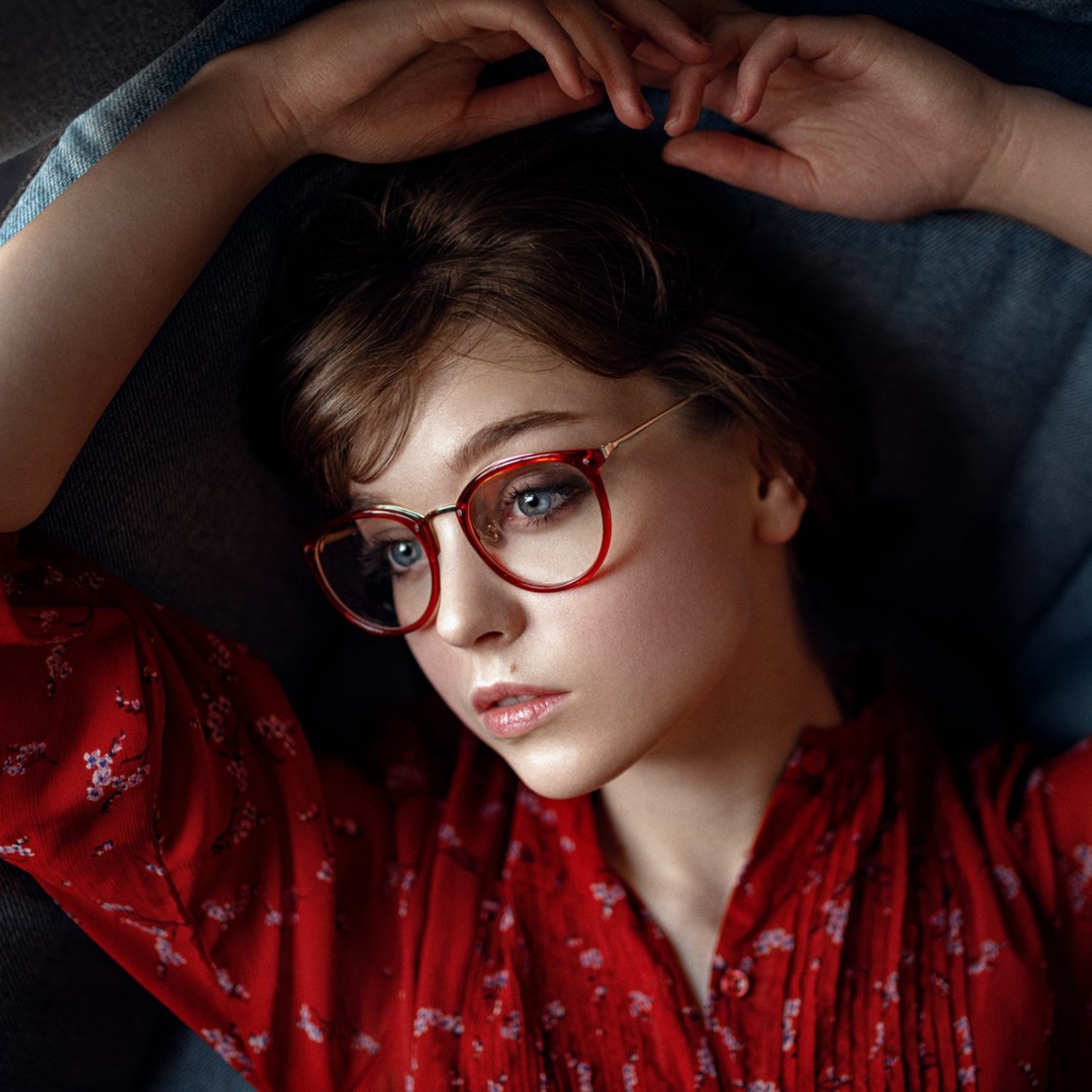 Молодая девушка в очках лежит на диване 