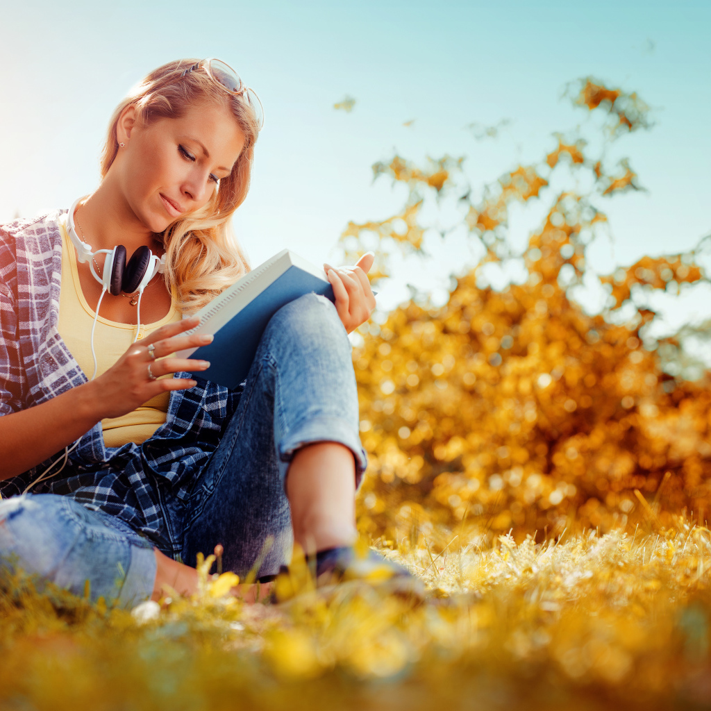 Молодая девушка читает книгу на желтой траве осенью