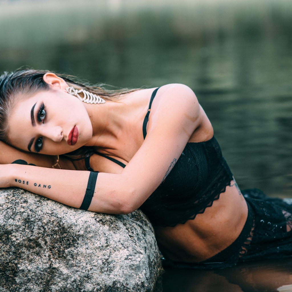 Молодая девушка с татуировками сидит у камня в воде