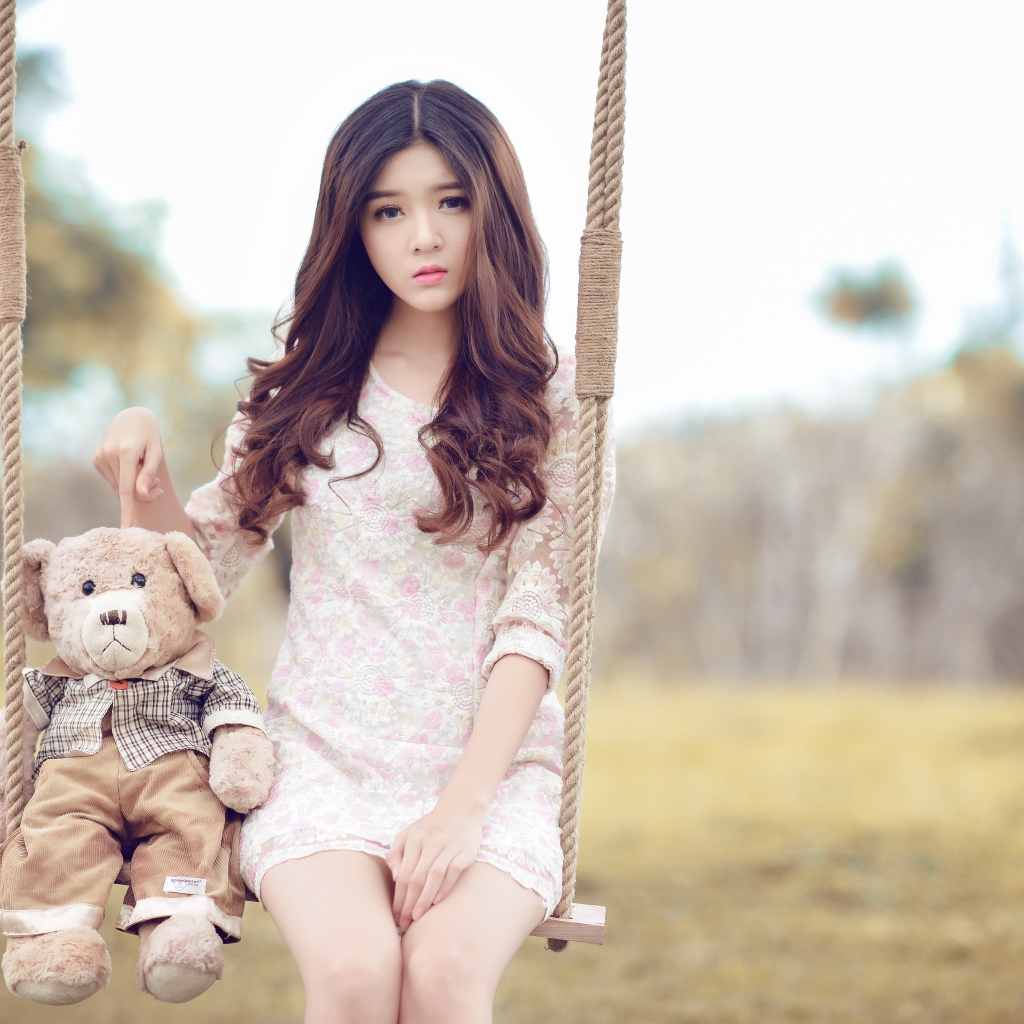 Девочка азиатка сидит на качели с плюшевым мишкой