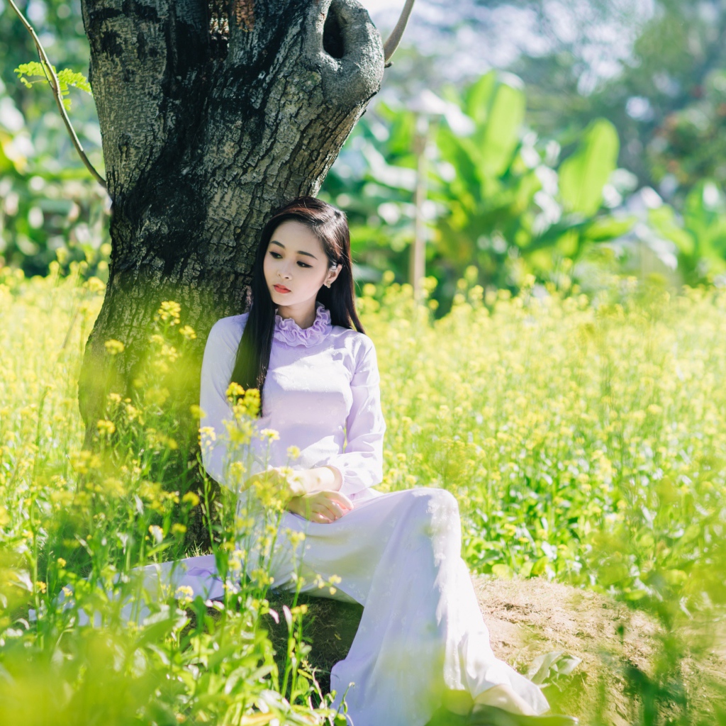 Красивая девушка азиатка сидит в белом платье под деревом