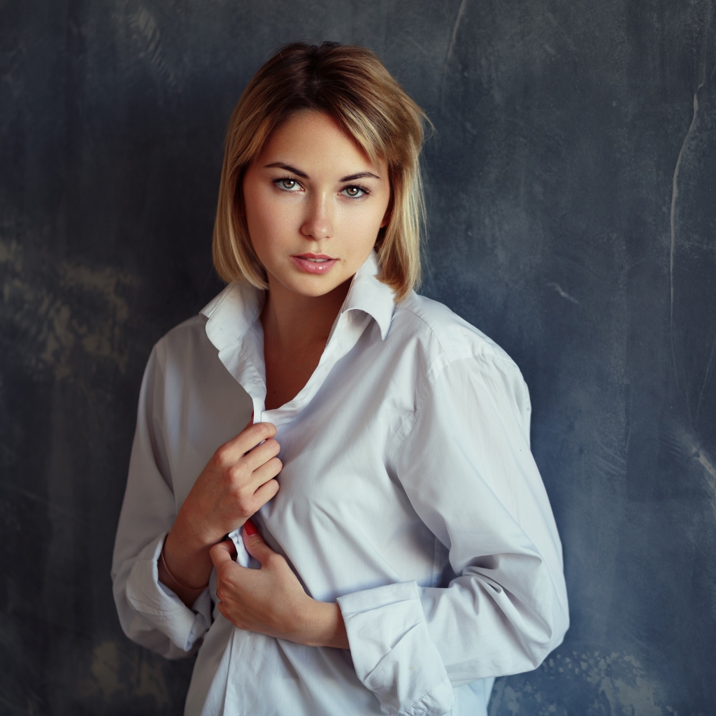 Красивая девушка блондинка в белой рубашке у стены 