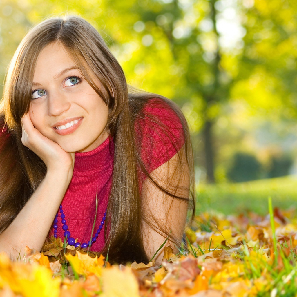 Красивая голубоглазая шатенка лежит на траве с желтыми листьями