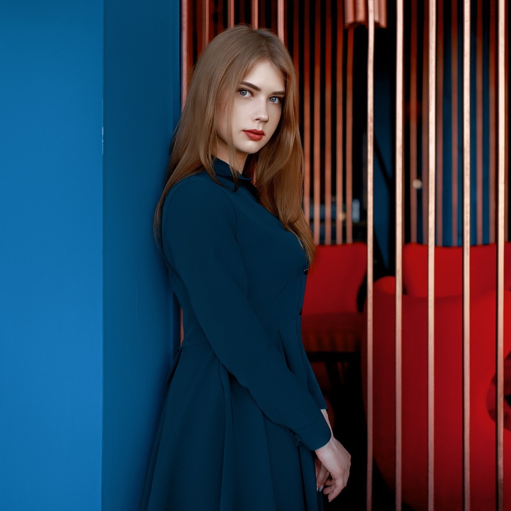 Красивая голубоглазая девушка стоит в пальто у стены