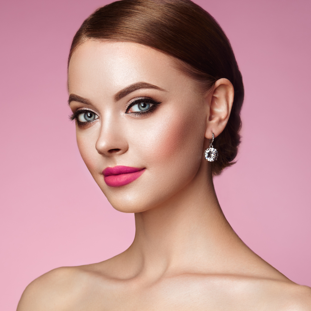 Красивая голубоглазая девушка с красивыми серьгами на розовом фоне